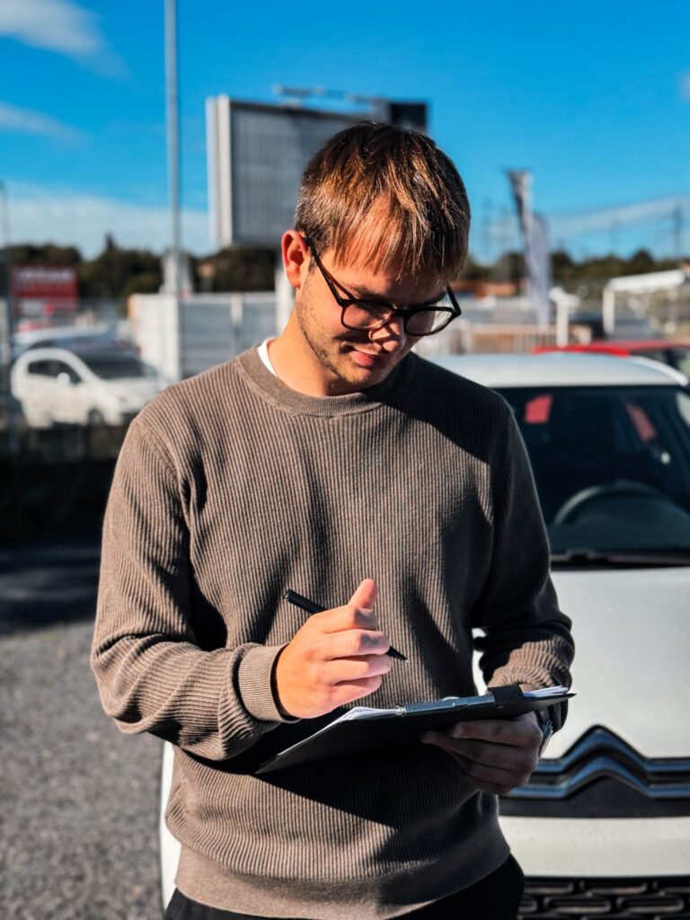 Émilien consultant les fiches d'inspection devant notre parc de véhicules d'occasion.